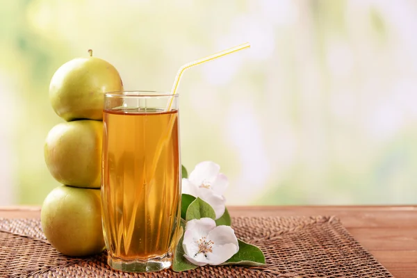 Glass of apple juice and apples on wooden table, on nature background — Stock Photo, Image