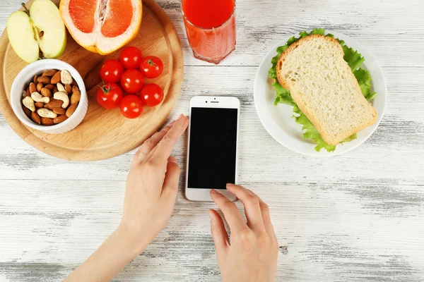 Gıda ve ahşap arka plan üzerinde eller içinde hareket eden telefon