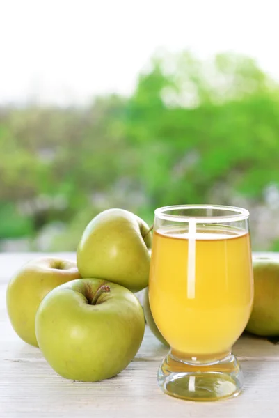 Sklenice jablečné šťávy a jablka na dřevěný stůl, na pozadí přírody — Stock fotografie