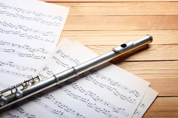 Flûte argentée avec notes de musique sur table en bois close up — Photo
