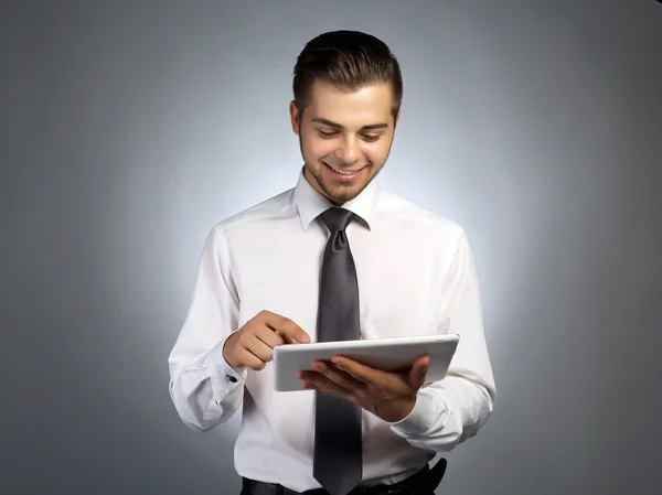 Hombre de negocios guapo sosteniendo la tableta sobre fondo gris — Foto de Stock