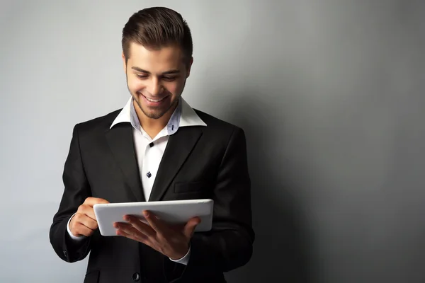 Knappe zakenman bedrijf tablet op grijze achtergrond — Stockfoto