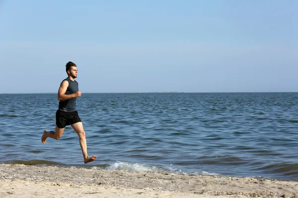 Ung man joggar på stranden — Stockfoto