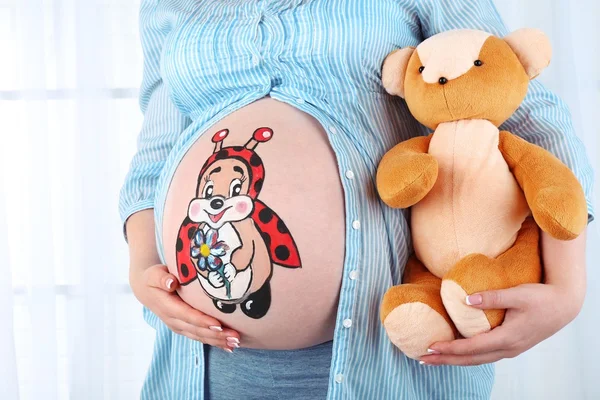 Belle jeune enceinte avec un jouet pour bébé et une image sur son ventre, sur fond clair — Photo