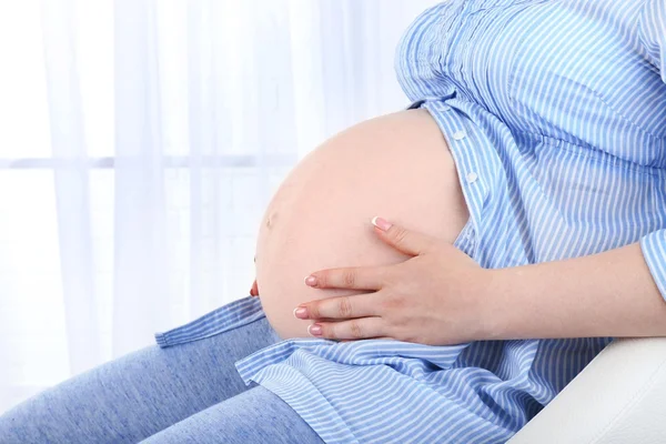 Vacker ung gravid kvinna röra hennes mage på ljus bakgrund — Stockfoto