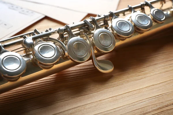 Silver flute with music notes on wooden table close up — Stock Photo, Image