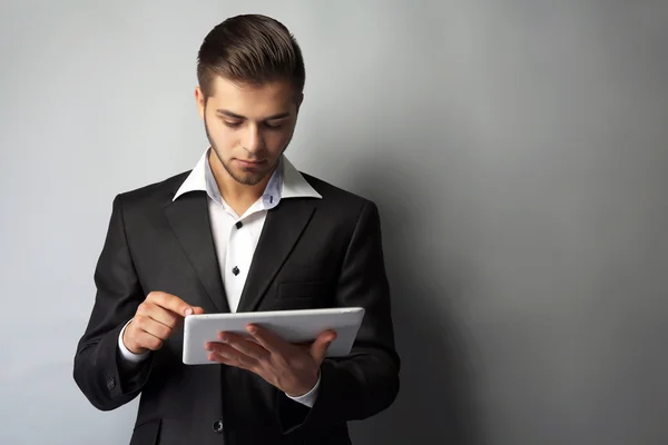 Schöner Geschäftsmann mit Tablet auf grauem Hintergrund — Stockfoto