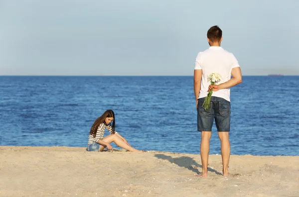 Young man giving flowers for his girlfriend on beach — 图库照片