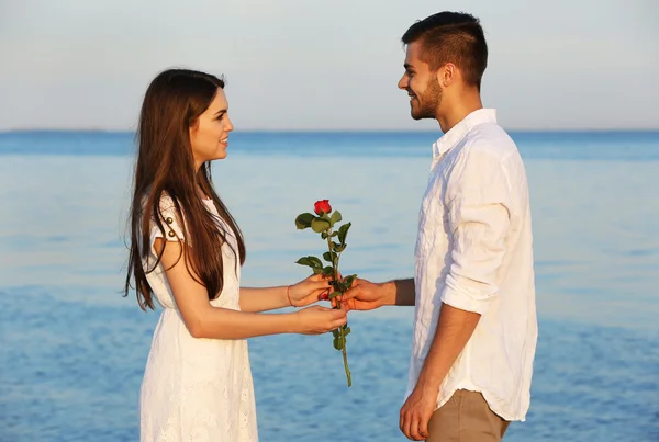Junger Mann schenkt seiner Freundin Blumen am Strand — Stockfoto
