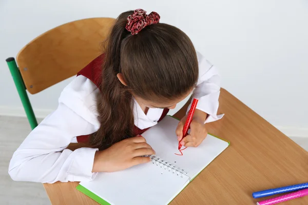 Belle petite écolière en classe et dessine dans un carnet — Photo
