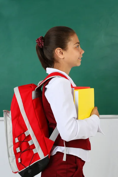 Beautiful little girl standing near blackboard in classroom — Stock Photo, Image