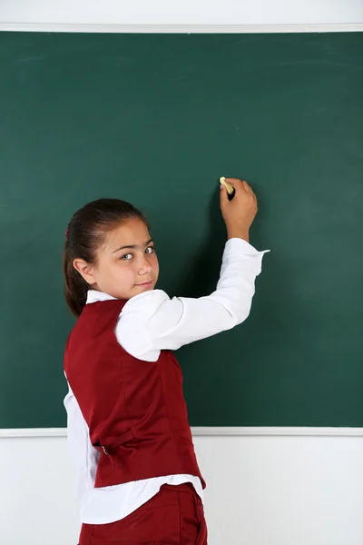 Beautiful little girl writes on blackboard in classroom — Stock Photo, Image