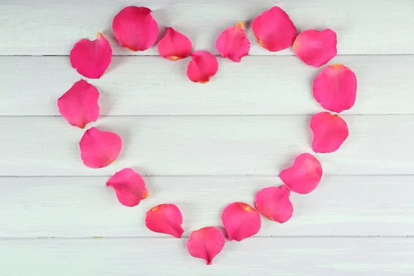 Coração de pétalas de rosa no fundo de madeira — Fotografia de Stock