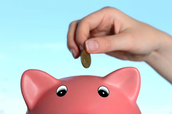 Hand inserting money into piggy bank on blue background Stok Resim