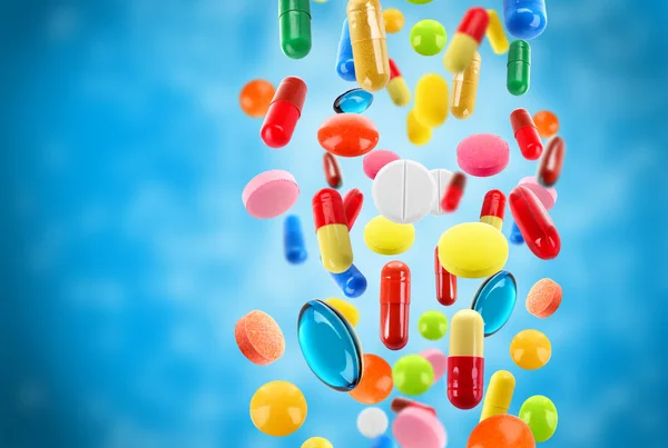 Caduta pillole mediche colorate su sfondo blu — Foto Stock