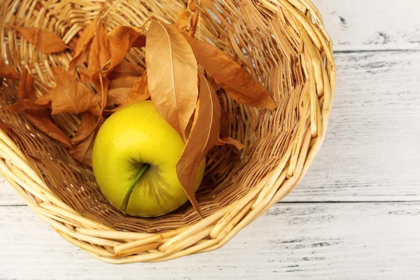 Apple with dried leaves in wicker basket on wooden background — Stock Photo, Image