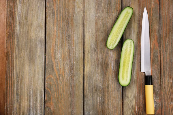 Halves of cucumber with knife on wooden background — Stock Photo, Image