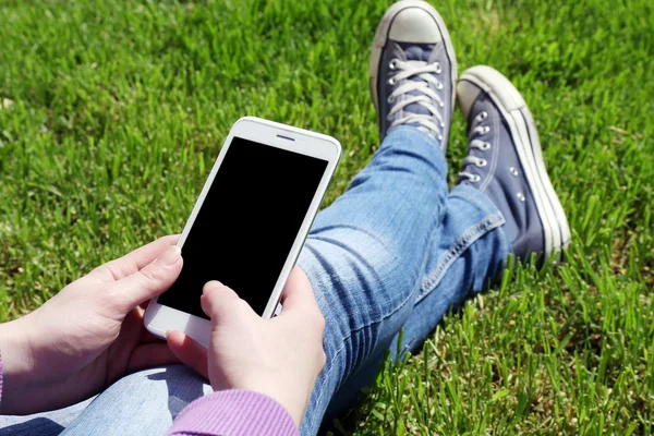 Cep telefonu açık havada yeşil çimenlerin üzerinde oturan genç kadınla — Stok fotoğraf