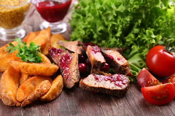 Carne com molho de cranberry, fatias de batata assadas na tábua de corte, no fundo de madeira — Fotografia de Stock