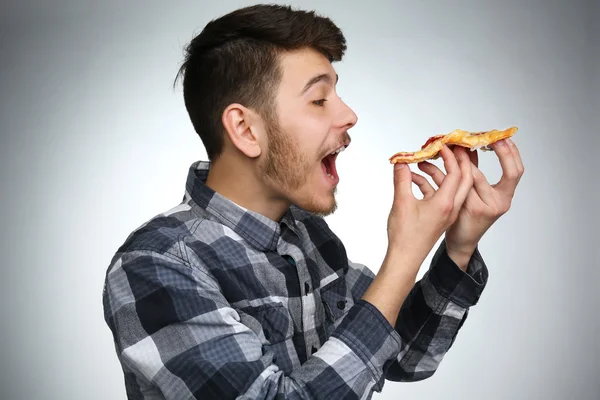 Fiatal ember eszik a darab pizza szürke háttér — Stock Fotó
