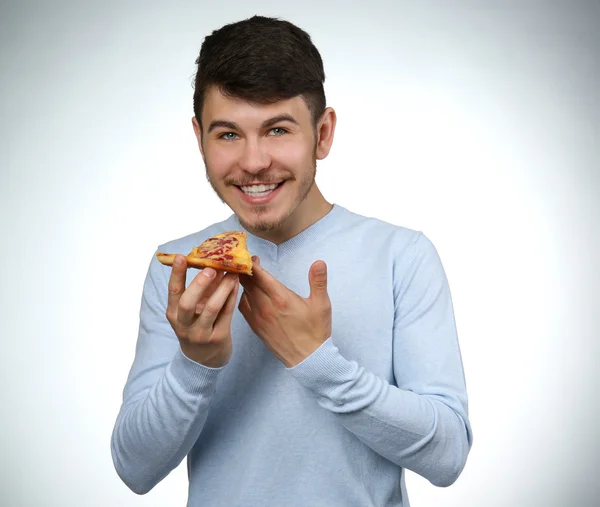 Jovem comendo pedaço de pizza no fundo cinza — Fotografia de Stock