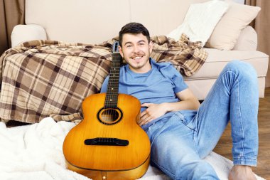 Gitarlı genç adam odada yerde yatıyor.