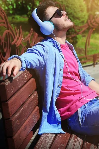 Uomo con cuffie poggiate su panchina nel parco — Foto Stock