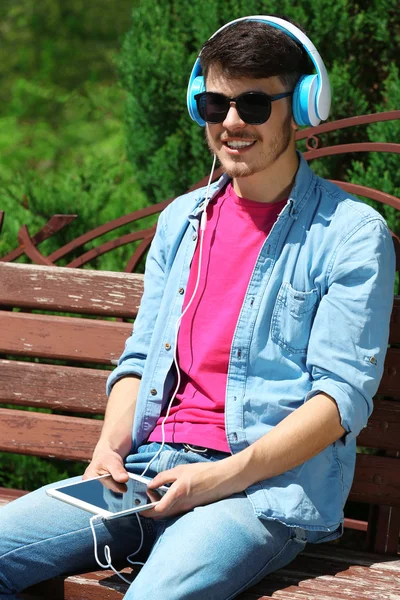 Άνθρωπος με ακουστικά που αναπαύεται σε παγκάκι στο πάρκο — Φωτογραφία Αρχείου