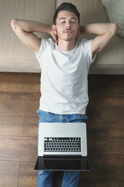 Young man sitting on floor with laptop in room — Stock Photo, Image