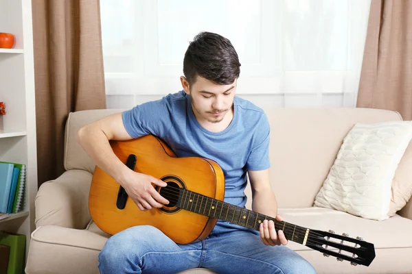 Νεαρός άνδρας με κιθάρα στον καναπέ στο δωμάτιο — Φωτογραφία Αρχείου