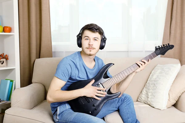 Young man with guitar on sofa in room — Stock Photo, Image