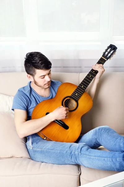 Joven con la guitarra en el sofá en la habitación — Foto de Stock