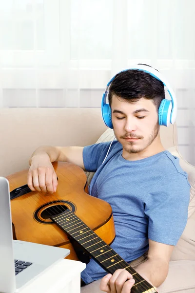 Mladý muž s kytarou na pohovce v pokoji — Stock fotografie