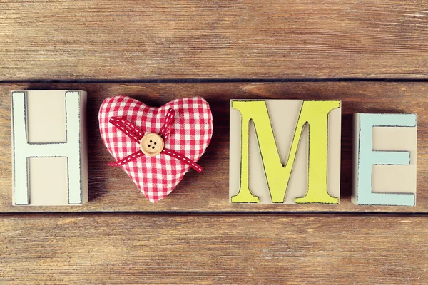Декоративні літери, що формують слово HOME з декоративним серцем на дерев'яному фоні — стокове фото