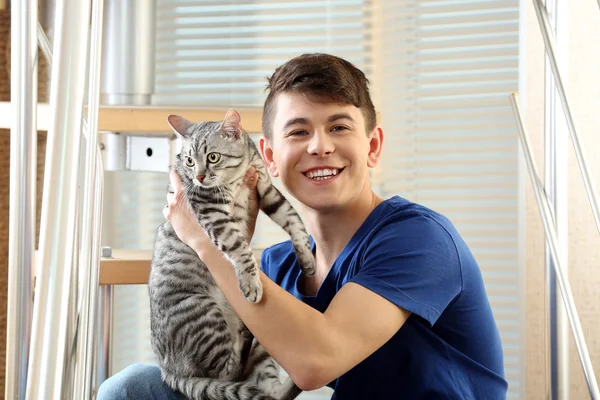 Schöner junger Mann mit süßer Katze sitzt auf Stufen zu Hause — Stockfoto