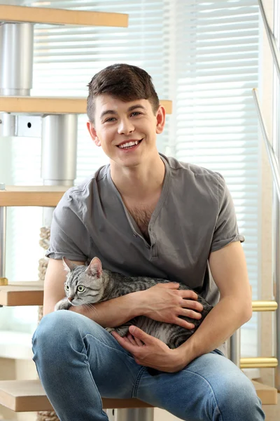 Beau jeune homme avec chat mignon assis sur les marches à la maison — Photo