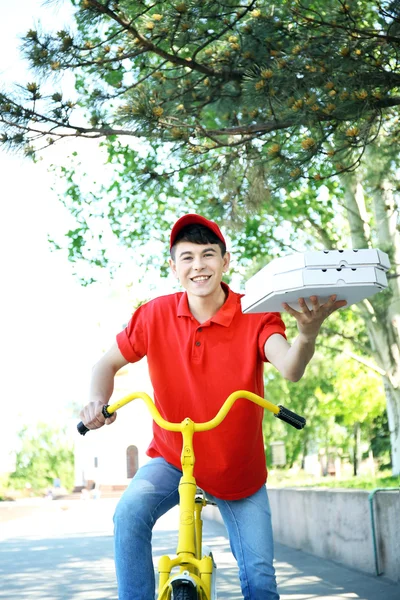 Hombre joven entrega caja de pizza en bicicleta al aire libre — Foto de Stock