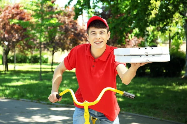 Молодой человек доставляет пиццу на велосипеде на открытом воздухе — стоковое фото