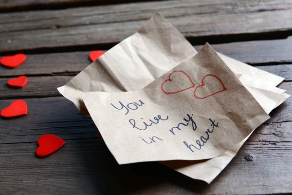 Written message with decorative hearts on wooden table close up — Stock Photo, Image