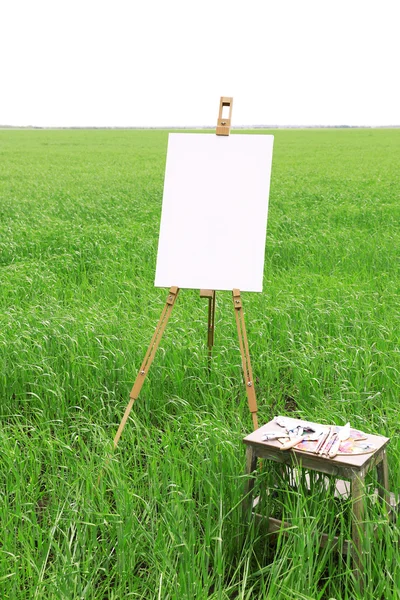 Staffelei mit Leinwand im grünen Feld — Stockfoto