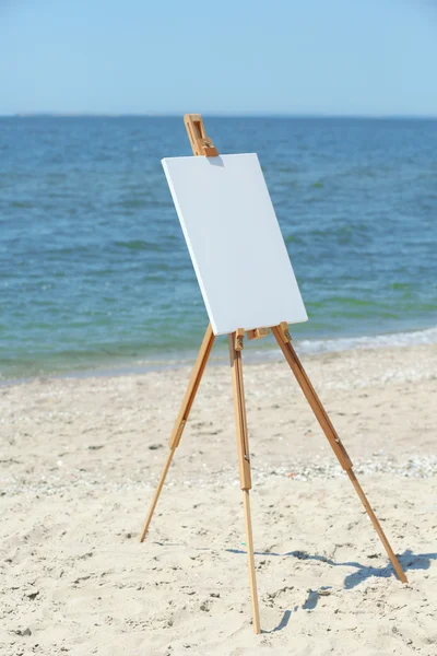 Weibliche Hand hält Palette mit Farben und Staffelei mit Leinwand am Strand — Stockfoto