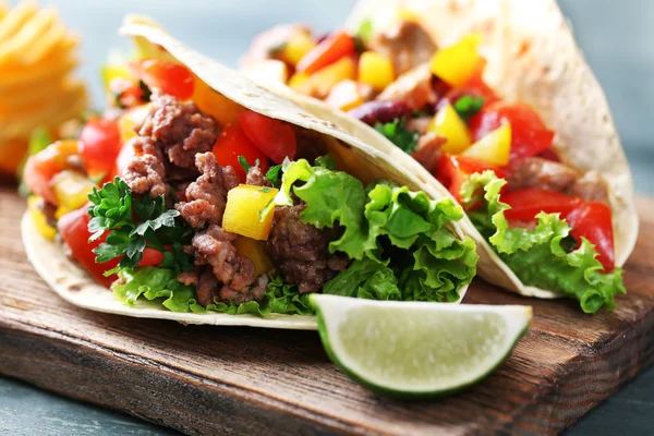 Burritos de carne caseira com legumes e tortilla, sobre tábua de corte, sobre fundo de madeira — Fotografia de Stock