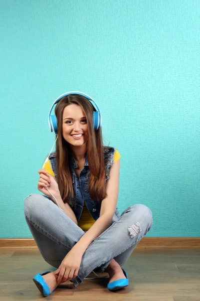 Young woman sitting on floor with headphones on turquoise wallpaper background — Stock Photo, Image