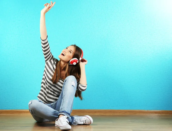 ターコイズ ブルーの壁紙の背景の上にヘッドフォンを床に座っていた若い女性 — ストック写真
