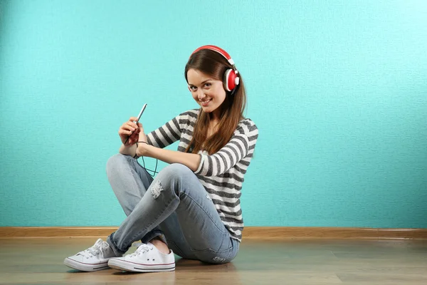 Young woman sitting on floor with headphones on turquoise wallpaper background — Stock Photo, Image