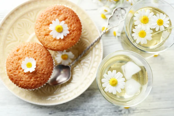 Szemüveg, kamilla tea, kamilla virágok és az ízletes muffinokat színes fából készült háttér — Stock Fotó