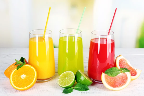 Vasos de diferentes jugos con frutas y menta sobre fondo brillante — Foto de Stock