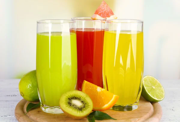 Vasos de diferentes jugos con frutas y menta sobre fondo brillante — Foto de Stock