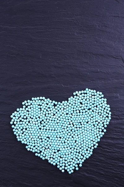 Colorful beads in heart shape on grey background — Zdjęcie stockowe