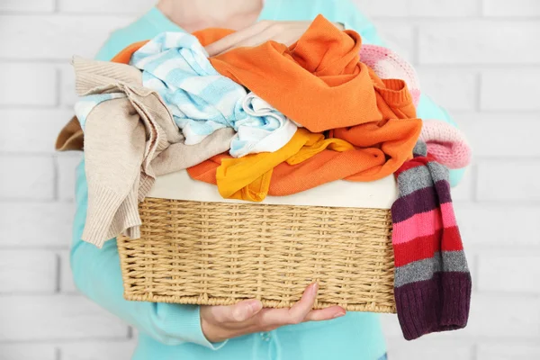 Mulher segurando cesta com montão de roupas diferentes, em tijolos fundo da parede — Fotografia de Stock